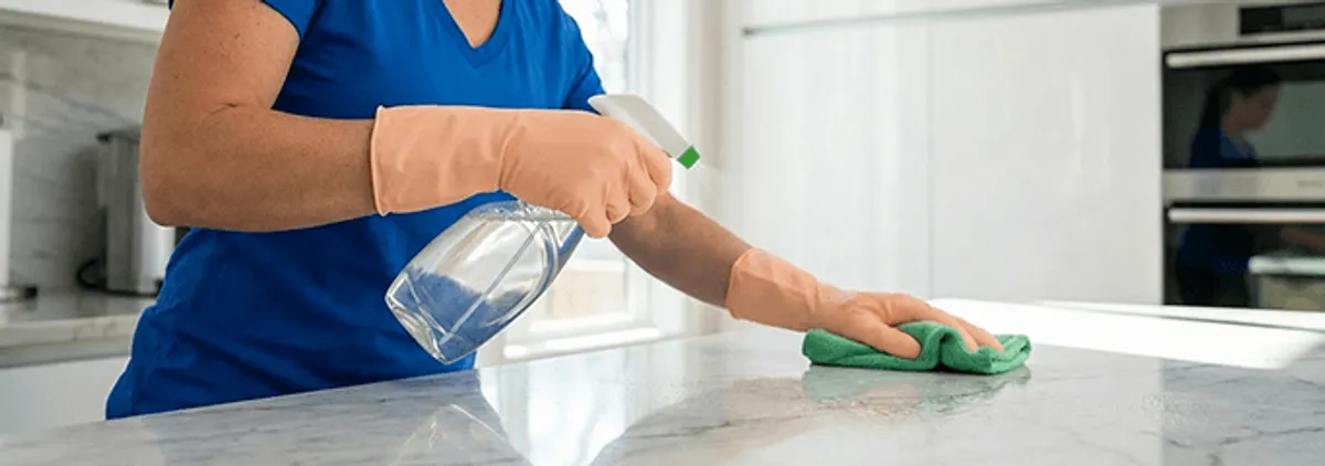 Maid service worker spraying and wiping a kitchen countertop with a microfiber cloth for sanitizing, Shreveport, LA.